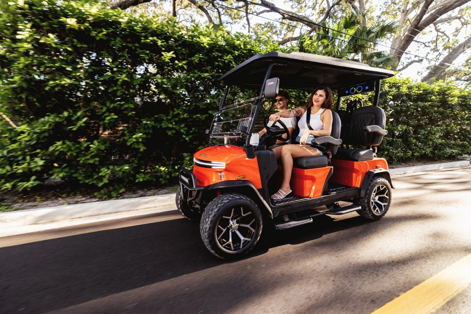 Couple cruising under live oaks in an orange Denago