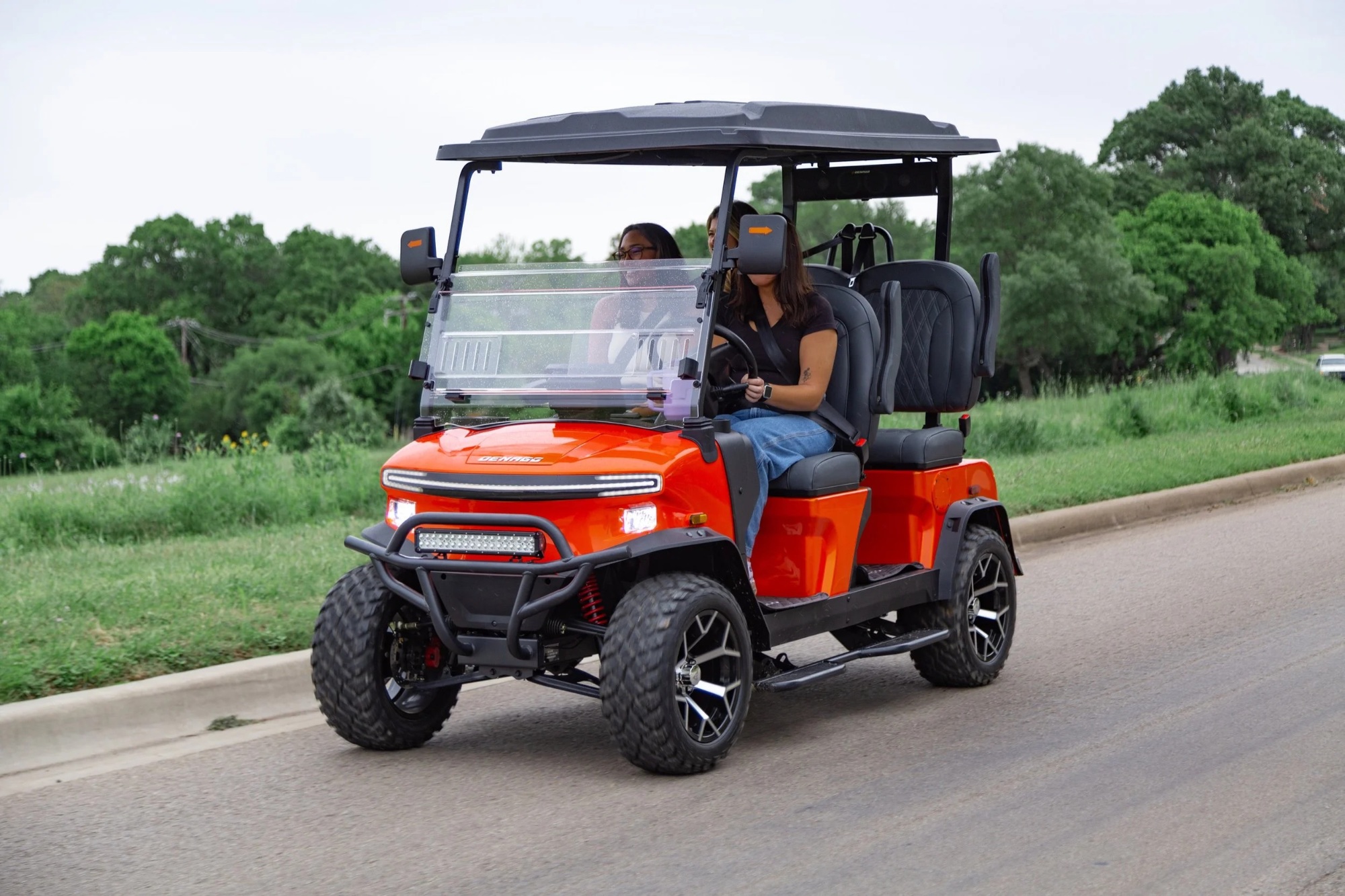 Orange Denago EV on a tree-lined road